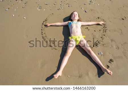 Little girl, closing her eyes, making sand angel on beach of Belek in Turkey
