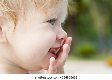 Little Girl Closing Her Mouth By Hand While Laughing. Close-up Portrait Of A Pretty Blond European Child.  Perfect Facial Features Of An Amazing Toddler. Expressing Emotions. Colorful Photo.