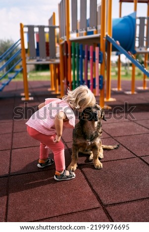 Little girl clung her head to a sitting dog on the playground