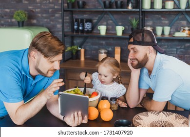 Little Girl Cooking A Salad While Her Father Give Instructions. Warm Atmosphere Of Love And Fathers' Care. LGBT Family With Kids.