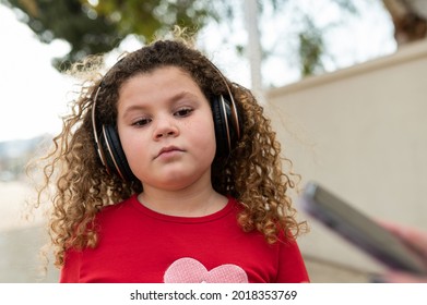 Little Girl In Cool Attitude Wearing Headphones In Public Park.