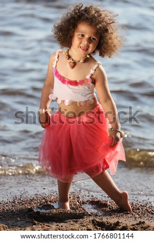 little girl with curly hair on the beach in a pink skirt