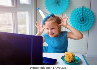 A little girl, curves and laughs in front of a laptop in a cap. Celebrates birthday via internet in quarantine time, self-isolation and family values, online birthday. Congratulations to the animator  - Powered by Shutterstock