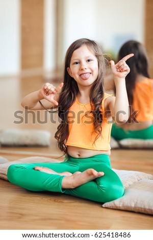 Little girl cute smiling, in sports clothes, in an orange top, shows a tongue