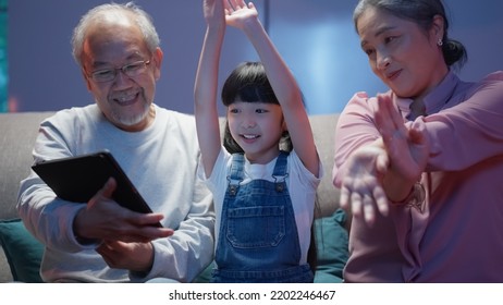 Little Girl Dancing With Family At Home, Cheerful Granddaughter Enjoying To Listen And Watch Music Video With Grandparents, Senior Grandparents Having Activities With Grandchild At Home Happily