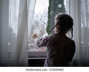 Little Girl Decorates The Window. Paste Paper Snowflakes. Child Is Waiting For The New Year Holiday