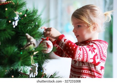 Little Girl Decorating Christmas Tree With Toys And Baubles. Cute Kid Preparing Home For Xmas Celebration.