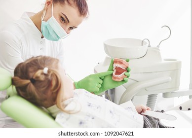 Little girl in dentists chair, being educated about proper tooth-brushing by her paediatric dentist. Early prevention and oral hygiene concept.