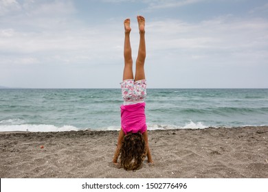 Little girl doing handstand on sand beach by the ocean - Powered by Shutterstock