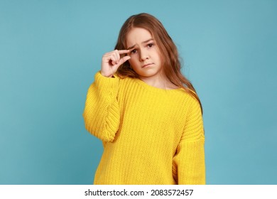 Little Girl Doing A Small Gesture, Looking With Displeased Imploring Expression, Shows Minimum, Wearing Yellow Casual Style Sweater. Indoor Studio Shot Isolated On Blue Background.