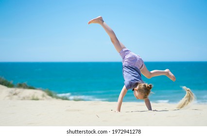 Little girl doing somersault on the beach. Outdoor games