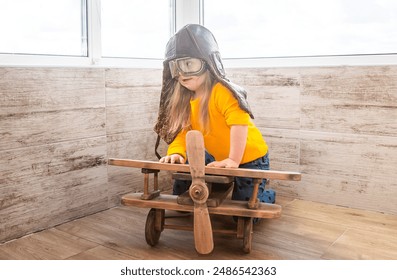 A little girl with down syndrome sitting near a wooden model of an airplane and wearing a pilot's helmet. Children with disabilities and health conditions. - Powered by Shutterstock