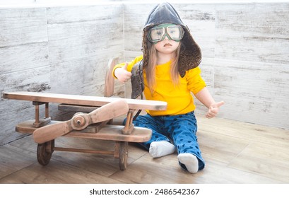 A little girl with down syndrome sitting near a wooden model of an airplane and wearing a pilot's helmet. Children with disabilities and health conditions. - Powered by Shutterstock