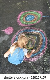 A Little Girl Is Drawing On The Ground With Chalk