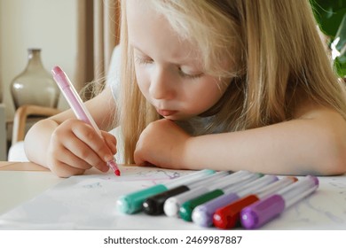 A little girl draws with a pink felt-tip pen on a white piece of paper. Lots of colored markers. - Powered by Shutterstock