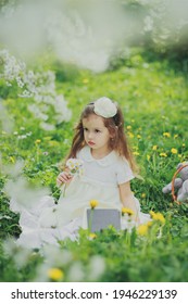 Little Girl In Dress Holding Bouquet Of White Daisies In Spring Cherry Garden. Portrait Of Sad Child Among White Flowers Trees. Childhood. Young Lady Sitting And Reading Book In Sunny Blooming Park.