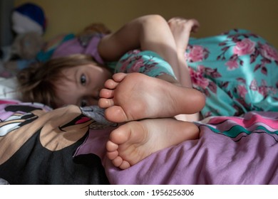 A Little Girl In A Dress Is Lying On The Bed. Focus On Bare Legs.