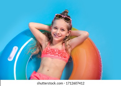 Little girl dressed in a swimsuit lying on an inflatable color ring on yellow background.