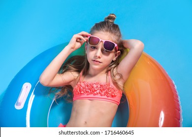 Little girl dressed in a swimsuit lying on an inflatable color ring on yellow background.