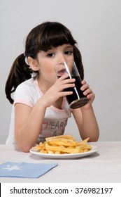 Little Girl Drinking A Glass Of Coke With A Plate Of French Frie