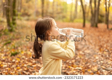 little girl drinking water from a bottle in the autumn forest on a sunny day
