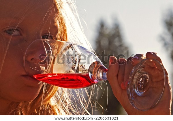 little girl drinks a red drink from a glass\
against the sun at a\
party.
