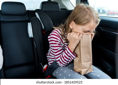 Little Girl Is Driving In Car. Kid Is Sick, Feels Bad And Vomiting Into Paper Bag. Traveling, Riding On Road In Safe Baby Seats With Child Belts. Fun Family Trip, Activity With Parents.