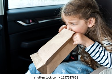 Little Girl Is Driving In Car. Kid Is Sick, Feels Bad And Vomiting Into Paper Bag. Traveling, Riding On Road In Safe Baby Seats With Child Belts. Fun Family Trip, Activity With Parents.