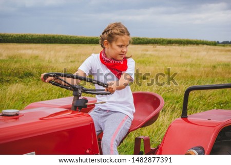 Little girl driving a red tractor. Agricultural work. Harvesting.