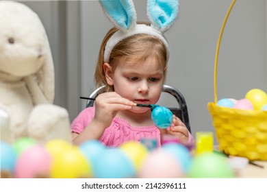 Little Girl In Easter Bunny Ears Painting Colored Eggs. Easter Family Holiday Celebration At Home And Craft Concept.