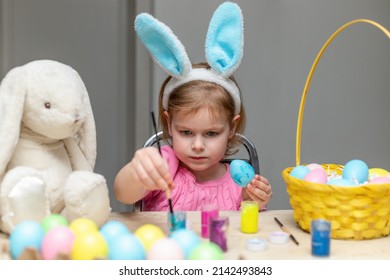 Little Girl In Easter Bunny Ears Painting Colored Eggs. Easter Family Holiday Celebration At Home And Craft Concept.