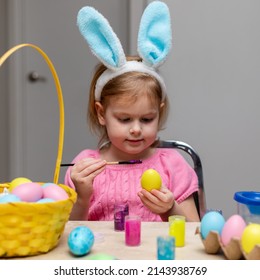 Little Girl In Easter Bunny Ears Painting Colored Eggs. Easter Family Holiday Celebration At Home And Craft Concept.