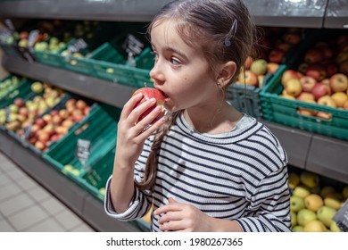 Little Girl Eating An Apple From The Counter At The Grocery Store.