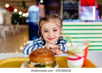 Little Girl Eating Hamburger And French Fries In A Fast Food Restaurant. Child Having Sandwich And Potato Chips For Lunch. Kids Eat Unhealthy Fat Food. Grilled Fastfood Sandwich For Children.