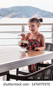 Little Girl Eating A Large Ice Cream Sundae With A Cherry On Top