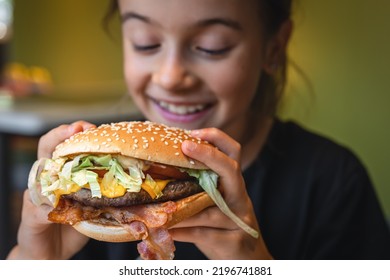 A little girl eats an appetizing burger, close-up. - Shutterstock ID 2196741881