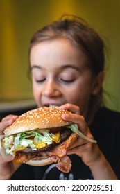 A little girl eats an appetizing burger, close-up. - Shutterstock ID 2200725151