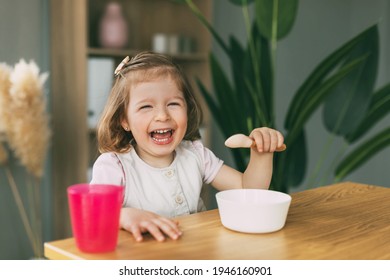A little girl eats porridge from a white bowl, a girl has breakfast sitting at the table. Healthy breakfast, healthy food
