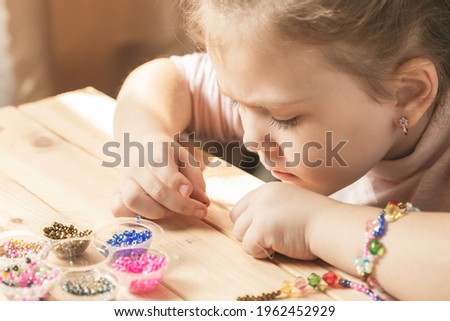 A little girl is engaged in needlework, making jewelry with her own hands, stringing multi-colored beads on a thread.
