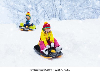 Little Girl Enjoying A Sleigh Ride. Child Sledding. Toddler Kid Riding A Sledge. Children Play Outdoors In Snow. Kids Sled In The Alps Mountains In Winter. Outdoor Fun For Family Christmas Vacation.