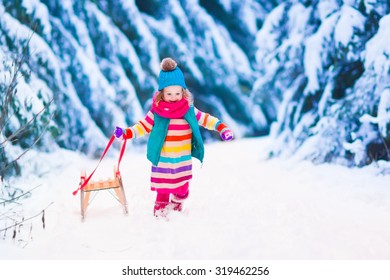 Little Girl Enjoying A Sleigh Ride. Child Sledding. Toddler Kid Riding A Sledge. Children Play Outdoors In Snow. Kids Sled In The Alps Mountains In Winter. Outdoor Fun For Family Christmas Vacation.