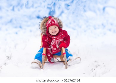 Little Girl Enjoying A Sleigh Ride. Child Sledding. Toddler Kid Riding A Sledge. Children Play Outdoors In Snow. Kids Sled In The Alps Mountains In Winter. Outdoor Fun For Family Christmas Vacation.