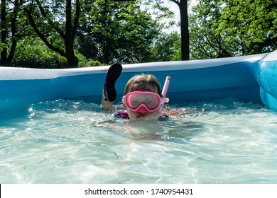 A Little Girl Enjoys Sunny Summer Fun, Swimming In A Backyard Kiddie Pool.