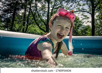 A Little Girl Enjoys Sunny Summer Fun, Swimming In A Backyard Kiddie Pool.