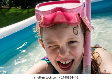 A Little Girl Enjoys Sunny Summer Fun, Swimming In A Backyard Kiddie Pool.