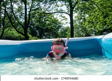 A Little Girl Enjoys Sunny Summer Fun, Swimming In A Backyard Kiddie Pool.