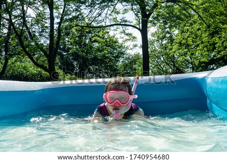 A little girl enjoys sunny summer fun, swimming in a backyard kiddie pool.
