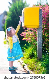 Little Girl With An Envelope At Post Office. Child Sending Letter. Kid Throwing Card Into A Mail Box. Postal Service In Germany, Europe. Delivery And Shipment At Outdoor Mailbox.