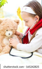 Little girl is examining her teddy bear using stethoscope