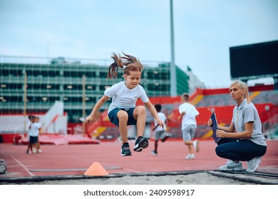 Little girl exercising long jump during sports training with her PE teacher at the stadium.  - Powered by Shutterstock